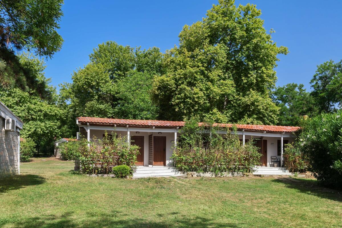 Une maison à deux étages, avec un toit recouvert de tuiles rouges, une véranda et une pelouse bien entretenue.