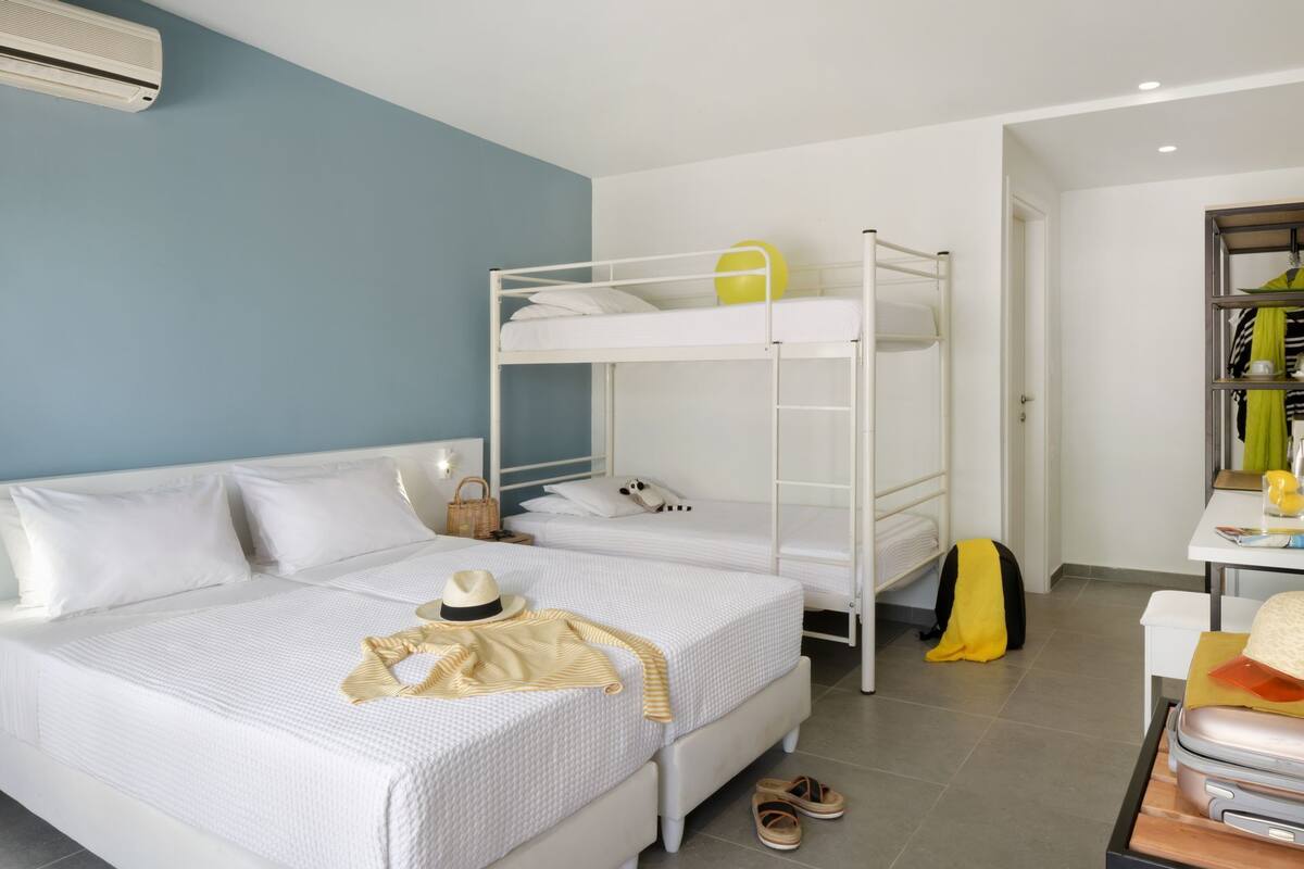 Une chambre avec un lit superposé, un lit blanc, une valise et un chapeau posés sur le lit.