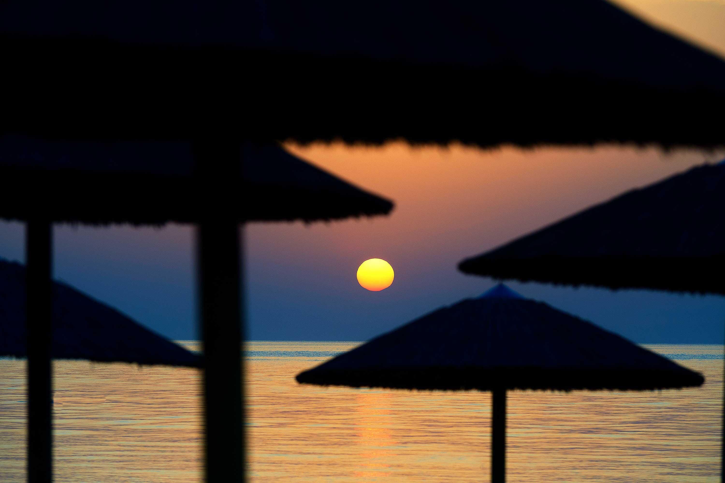 A sunset over water with beach umbrellas in the foreground.