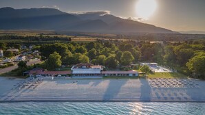 Vista aérea de una zona costera con un edificio grande, posiblemente un hotel, cerca de una playa con sombrillas y una piscina.
