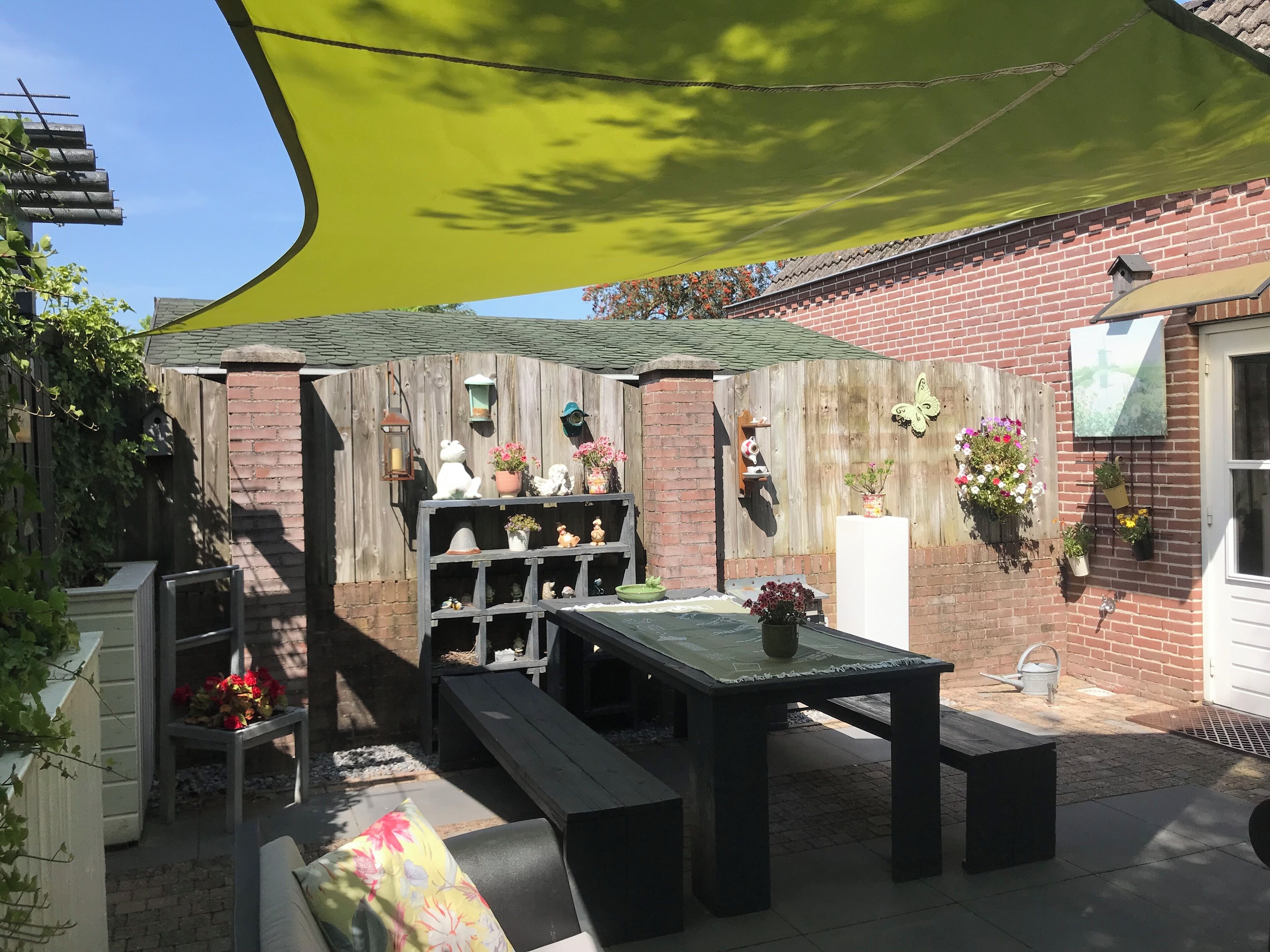Une terrasse avec une clôture en bois, une table, des bancs et diverses plantes en pot.