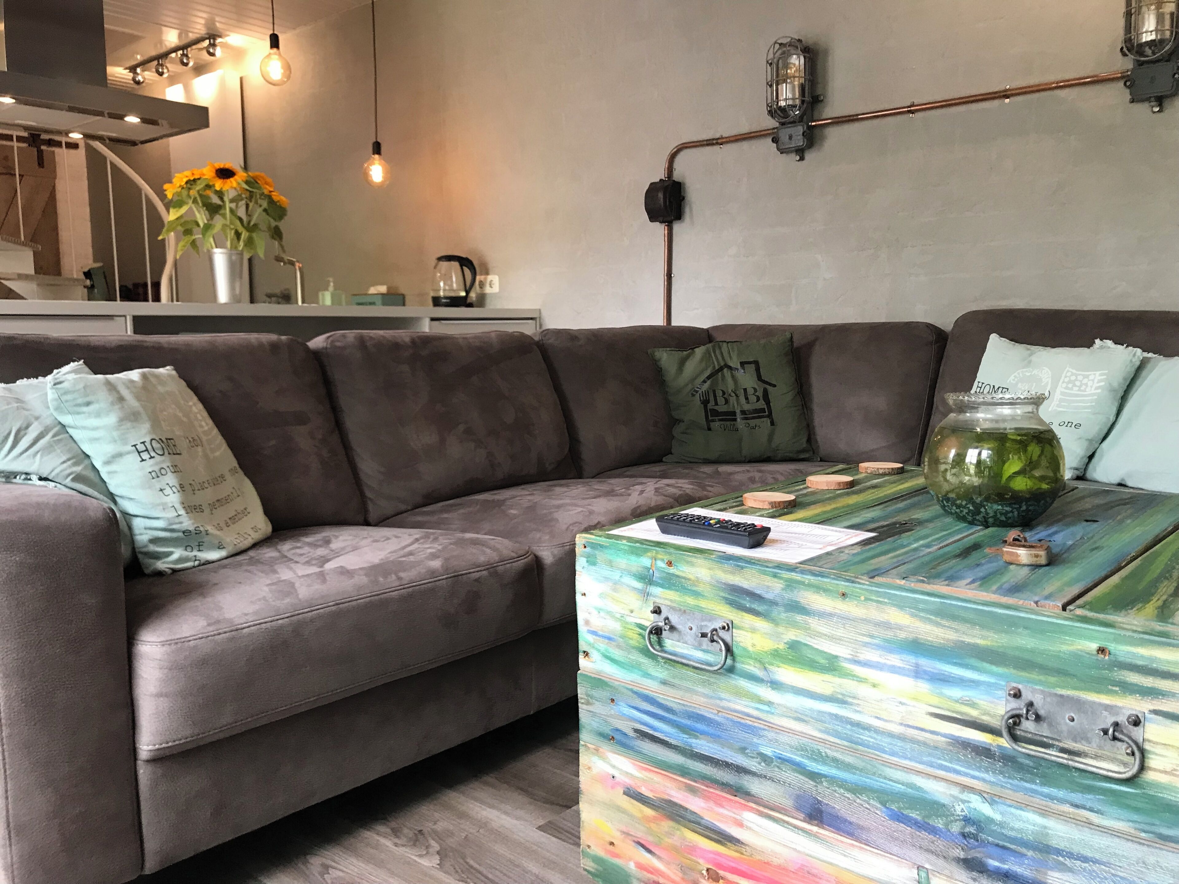 A modern living room with a grey sectional sofa, a colorful coffee table, and a vase with sunflowers.