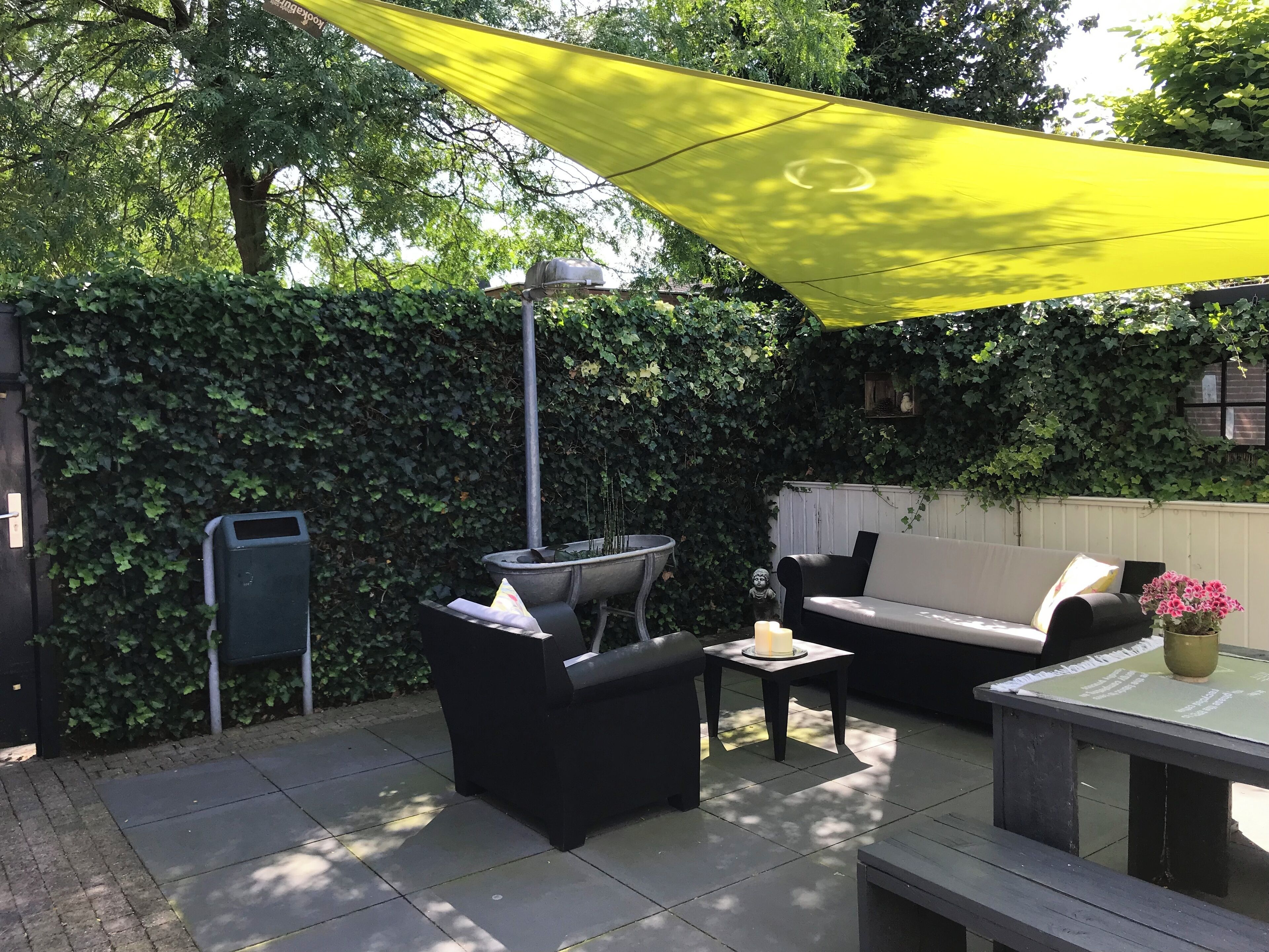 An outdoor patio area with a black sofa, a small table, a barbecue grill, and a yellow canopy.
