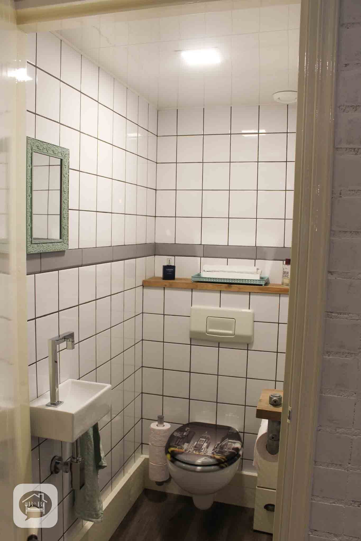 A small, tiled bathroom with a toilet, sink, and a mirror.