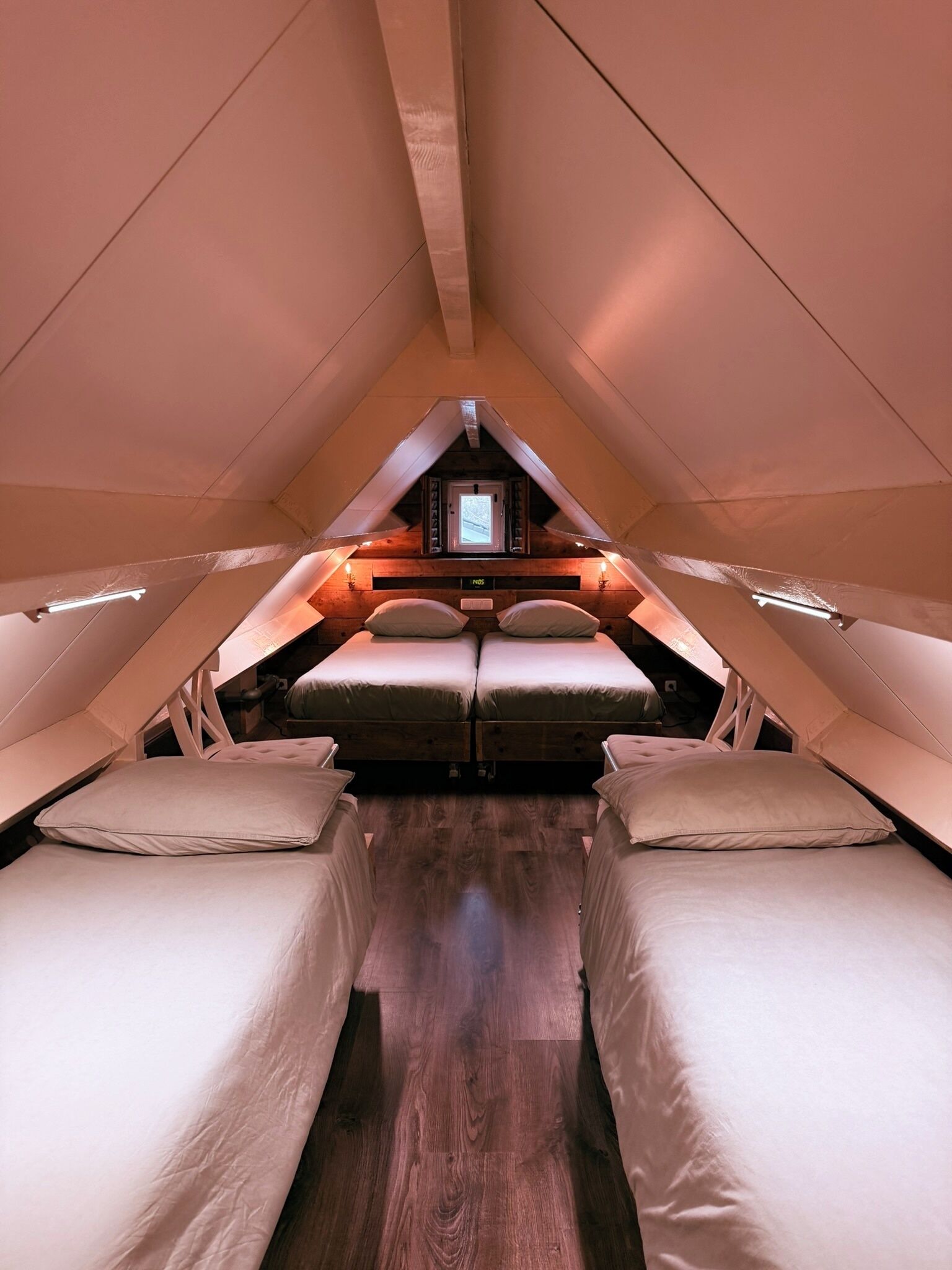 Un dormitorio acogedor en el ático, con dos camas, suelo de madera y una ventana pequeña.