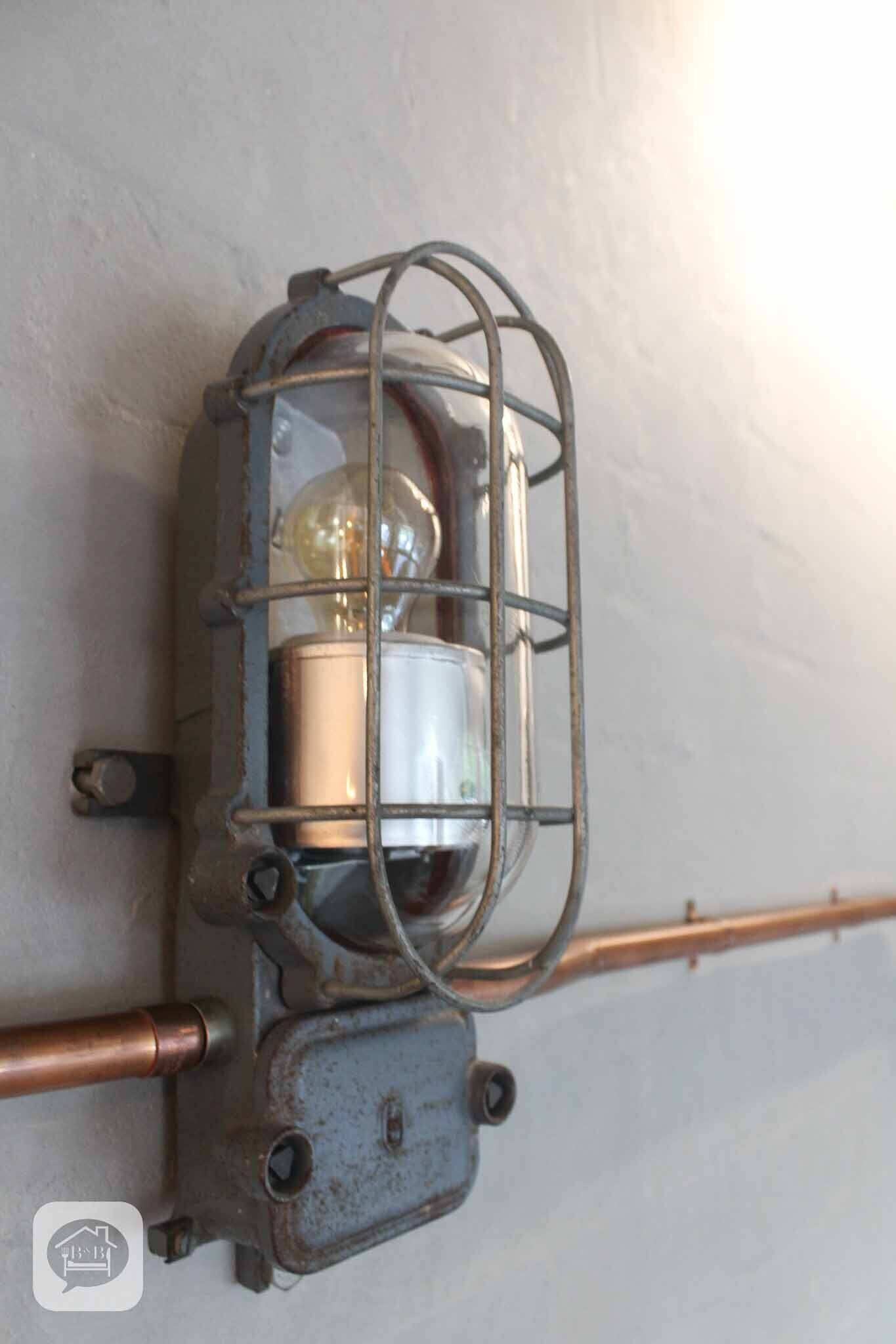 Eine altmodische Wandleuchte mit Glaskuppel und freiliegenden Kabeln.