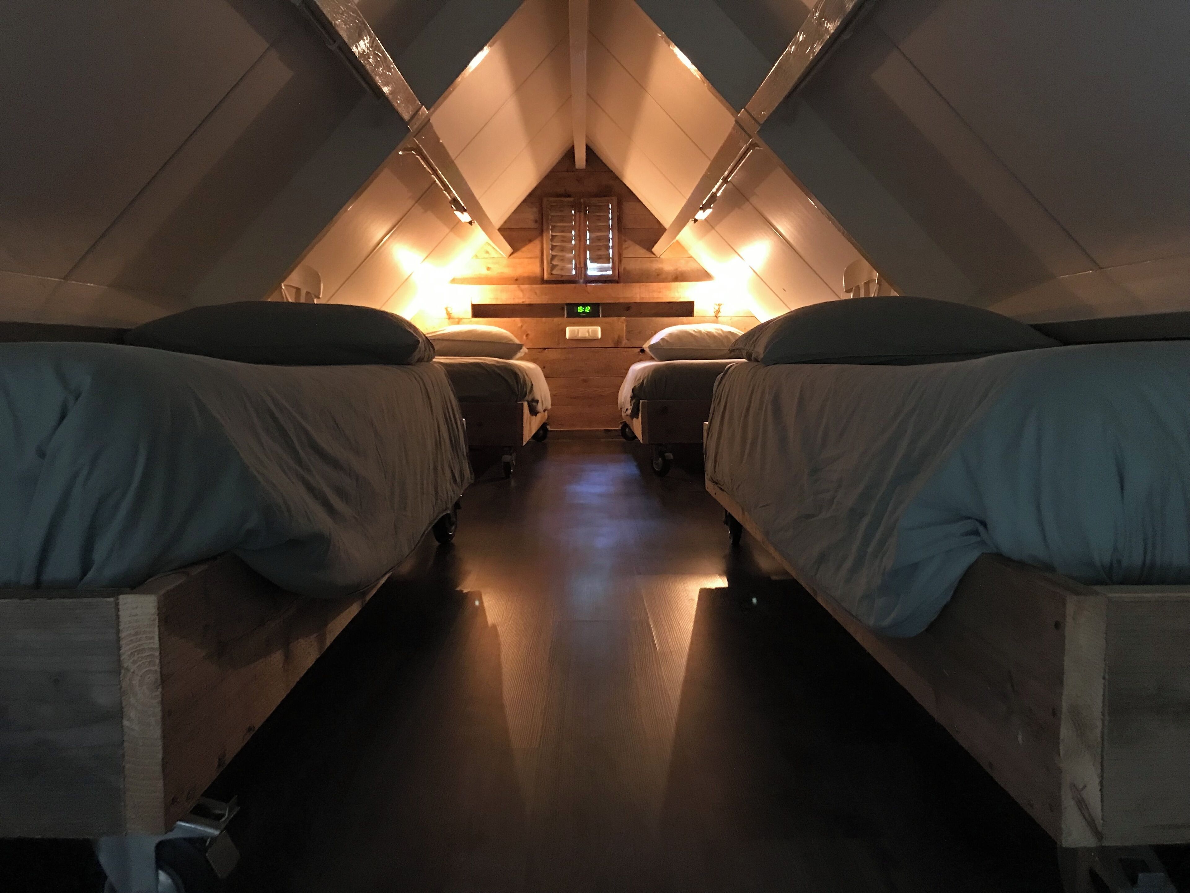 Une pièce avec quatre lits disposés en rangée, des murs en bois, un plafond en pente et une petite fenêtre au fond.
