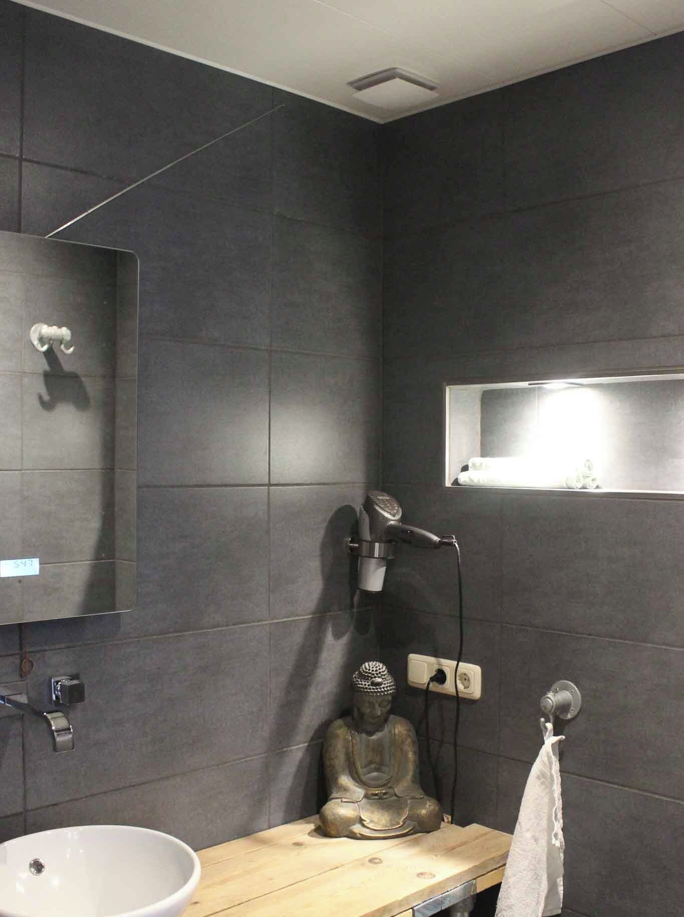 A modern bathroom with a large mirror, a sink, a hairdryer, and a statue.