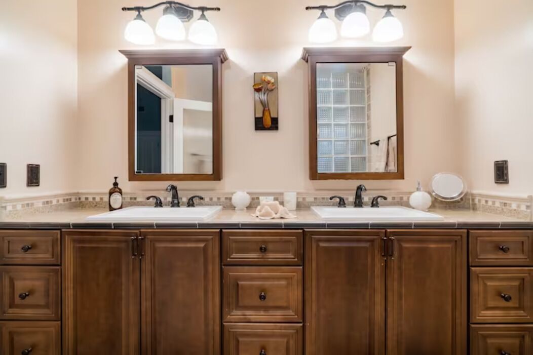A bathroom with two sinks, wooden cabinets, and a mirror with lights.
