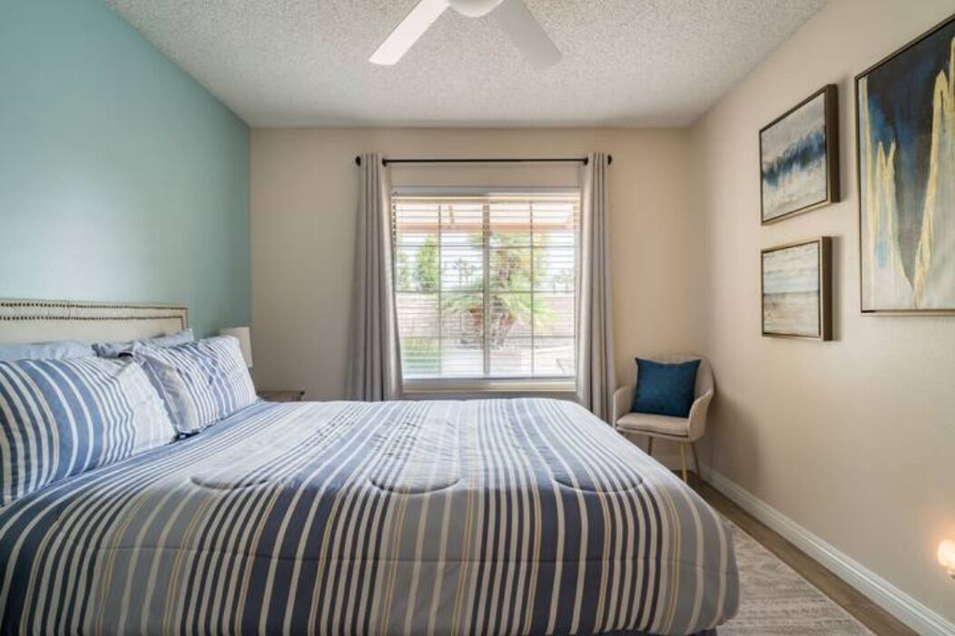 Un dormitorio con una cama grande, una ventana con cortinas, una silla y cuadros en la pared.