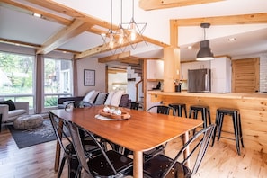 Un comedor amplio con una mesa y sillas de madera, una cocina con armarios blancos y un refrigerador de acero inoxidable, y un ventanal que ofrece luz natural.