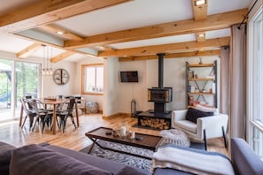 Un salón espacioso con techo de madera, chimenea, comedor y un ventanal grande.