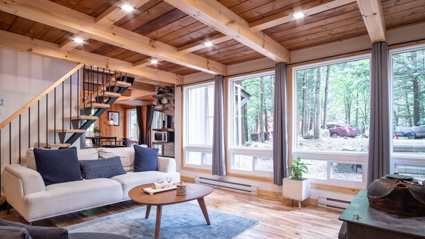 Ein modernes Wohnzimmer mit Treppe, großen Fenstern und Blick auf den Wald.