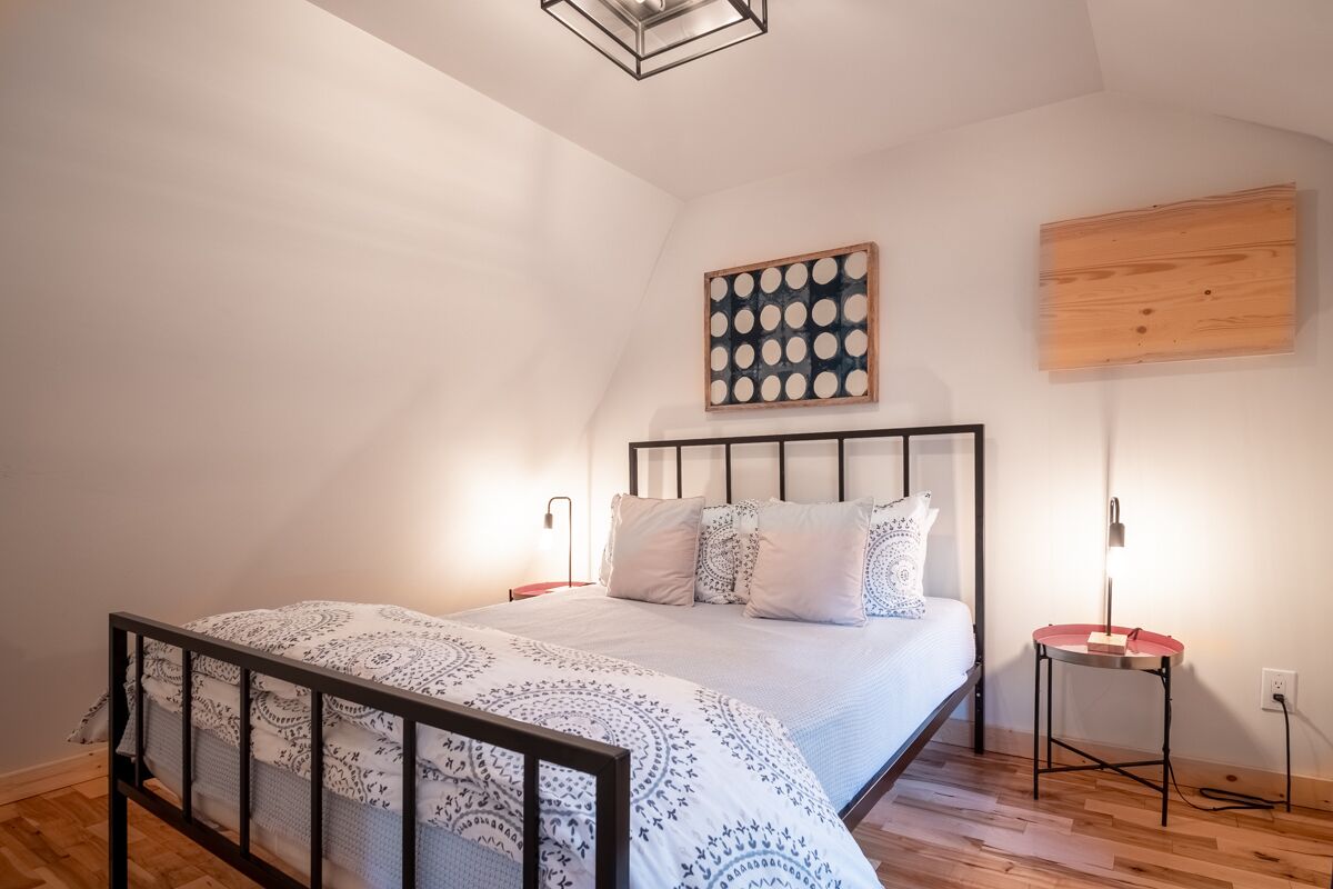 A bedroom with a bed, a nightstand, a wall-mounted artwork, and a wooden panel on the wall.