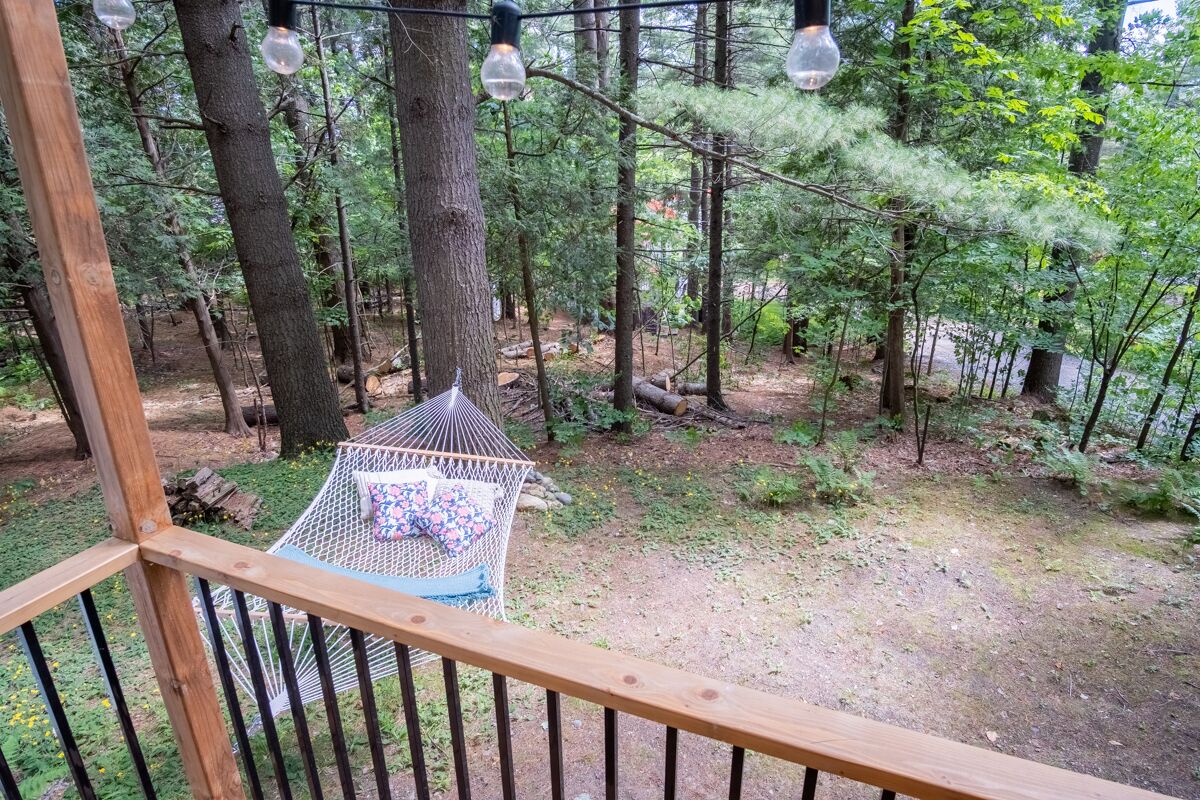 Un fauteuil suspendu, de type hamac, installé dans un espace boisé, avec une terrasse en bois et une rambarde en métal.