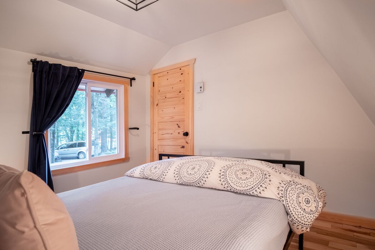 Une chambre à coucher avec un lit, une fenêtre avec des rideaux, une porte en bois et une vue sur des arbres et une voiture à l’extérieur.