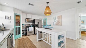 A modern kitchen with white cabinets, a central island, and a hanging light fixture. - Galveston Gem: Two Homes, Pool & More Amenities (Galveston)