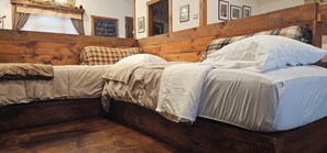 Una habitación con cabecera de madera, dos camas con ropa de cama color beige, una ventana con cortina y un cartel en la pared.