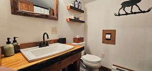 Un baño con lavamanos blanco, grifo negro, encimera de madera y espejo con marco rústico.