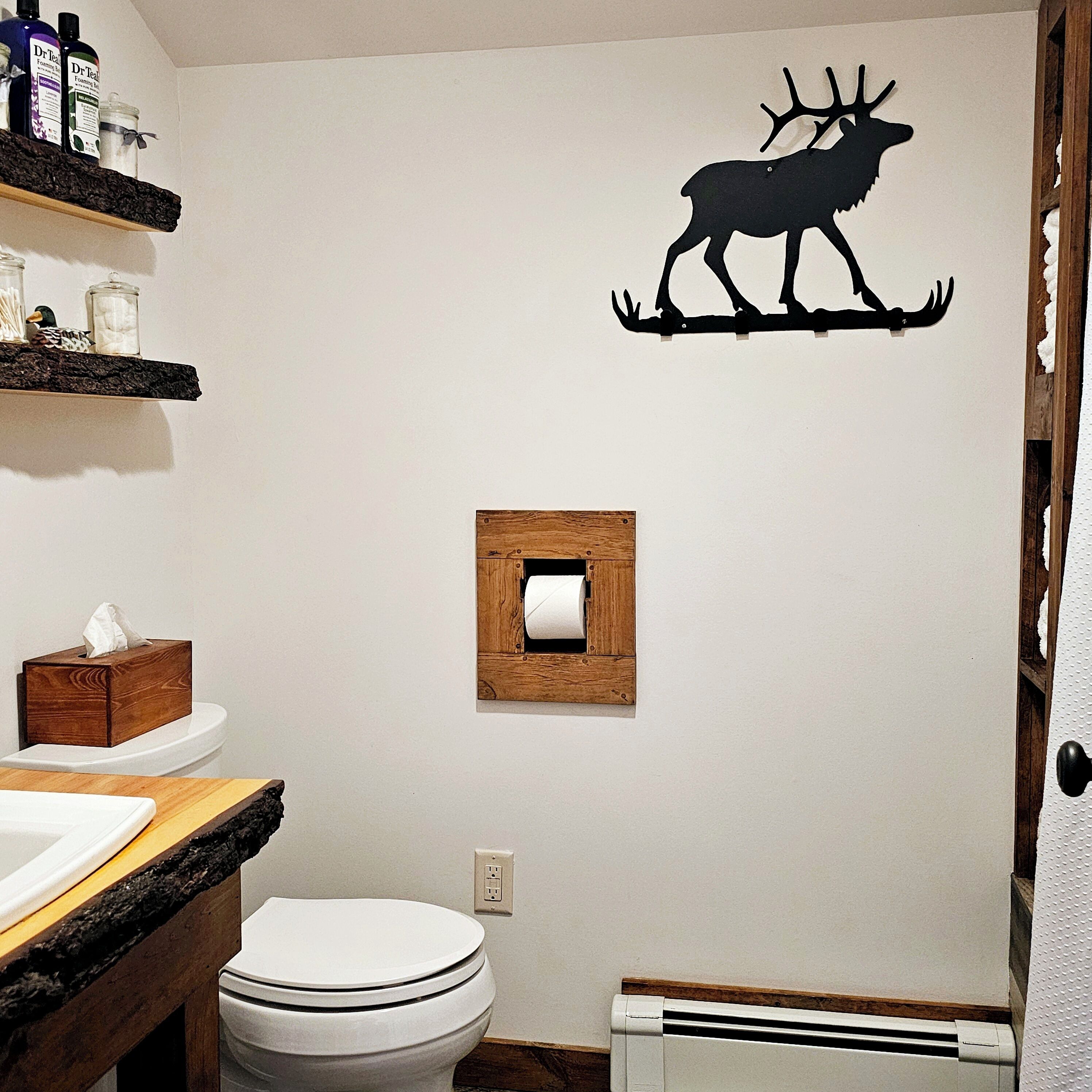 Casa de banho com sanita, lavatório, espelho, prateleira com produtos de higiene pessoal e um decalque de veado na parede.