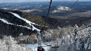 En skilift med passagerer, omgivet af sneklædte træer og et bjergrigt landskab.