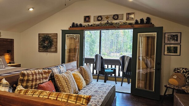 A cozy room with a bed, a sofa, and a balcony with chairs. - ADK Rustic Private Chalet Viewing Two Ponds / Forest 5.3 miles To Gore Mountain (North Creek)