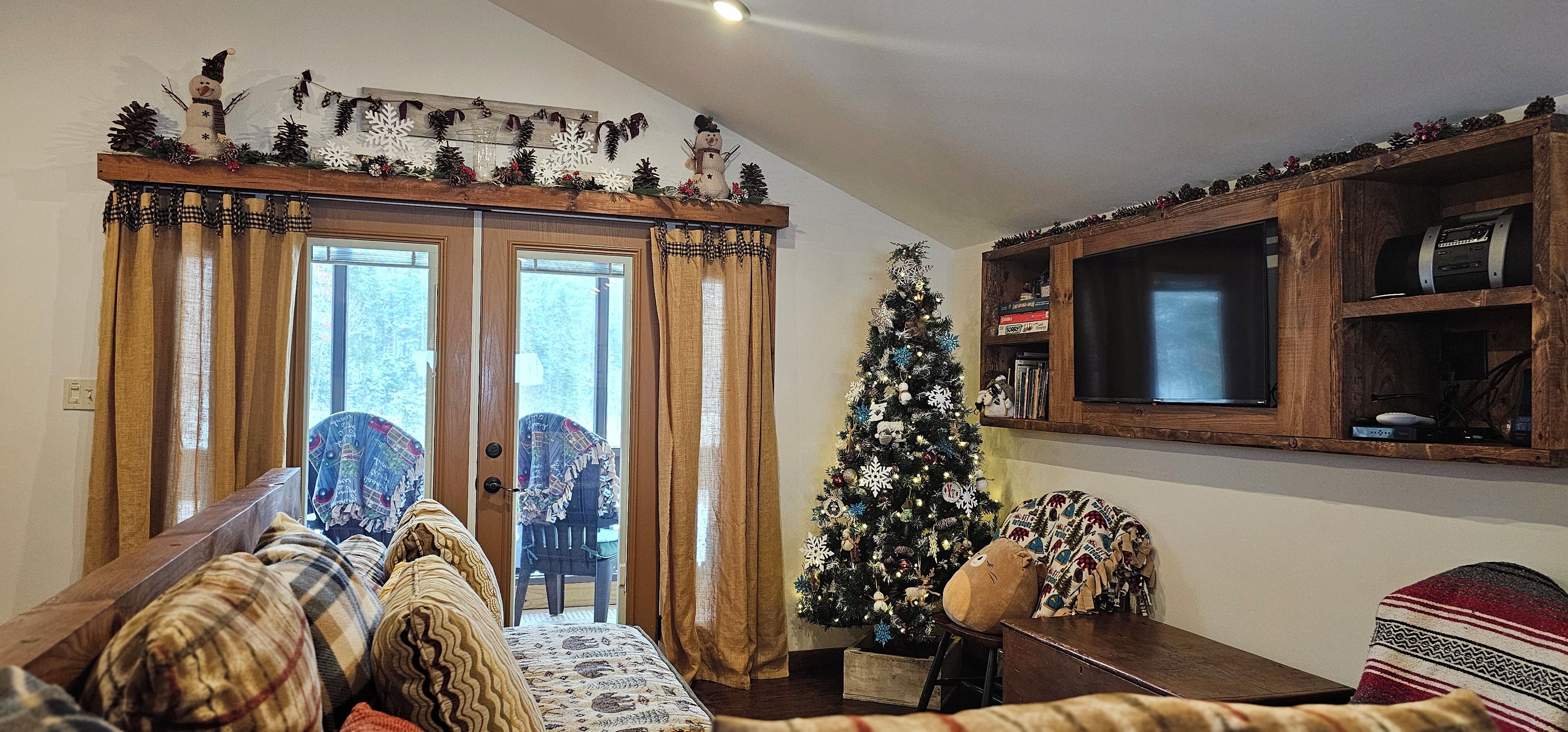 Un soggiorno accogliente con televisione a cornice di legno, albero di Natale e divano con cuscini decorati.