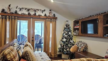 Un soggiorno accogliente con televisione a cornice di legno, albero di Natale e divano con cuscini decorati.