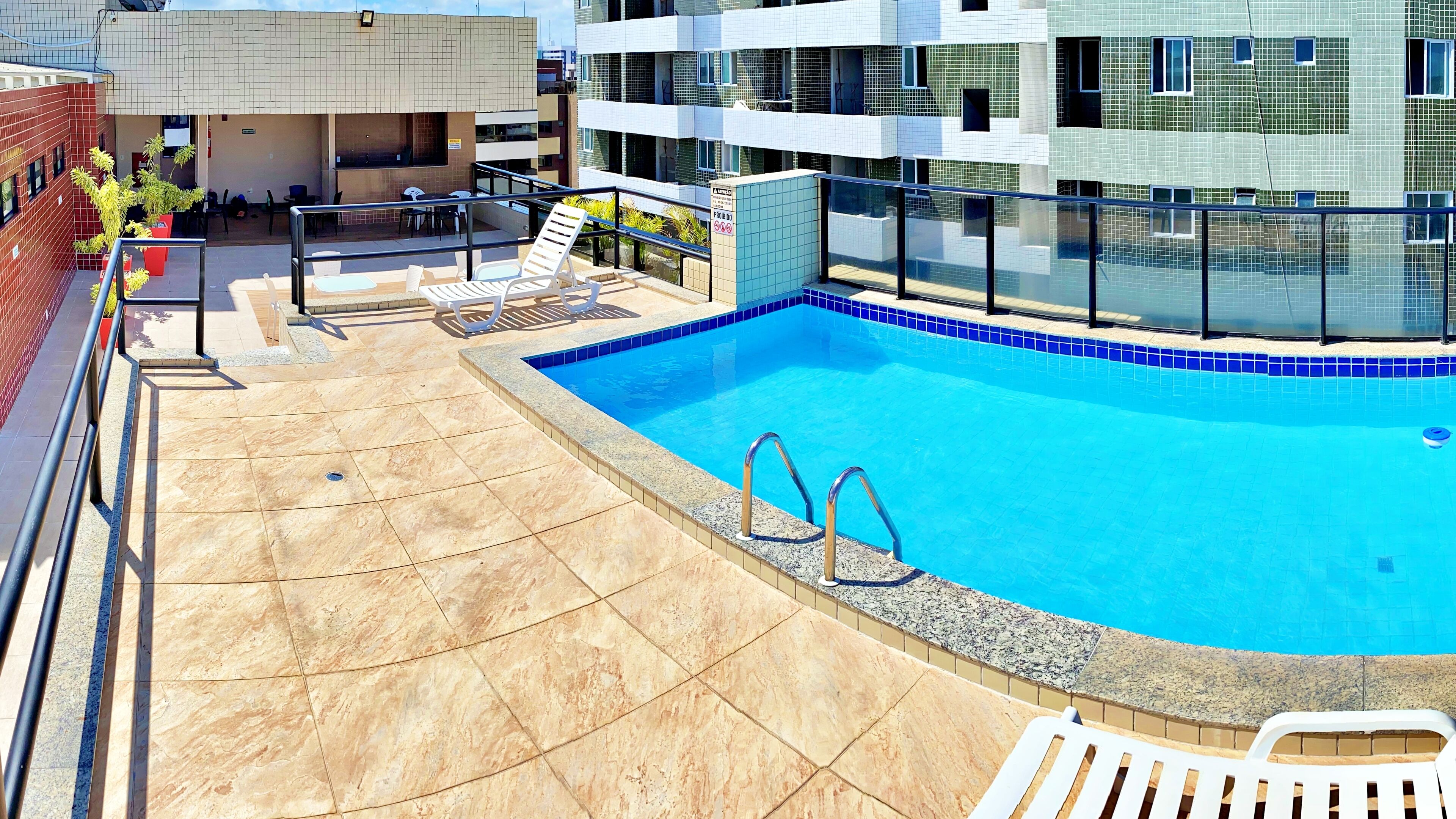 A swimming pool with a tiled deck, lounge chairs, and a glass-enclosed area.
