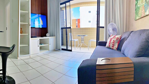A modern living room with a sofa, a TV, a small table, and a chair. - Vacanze - Monteverdi (Maceió)