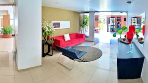 A modern living room with a red sofa, a black lounge chair, and a glass coffee table. There is a potted plant and a framed picture on the wall. - Vacanze - Monteverdi (Maceió)