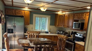A kitchen with wooden cabinets, a stainless steel refrigerator, a microwave, and a wooden dining table with chairs. - Cozy Chalet with First Lake access just minutes from town.  Great Location (Old Forge)