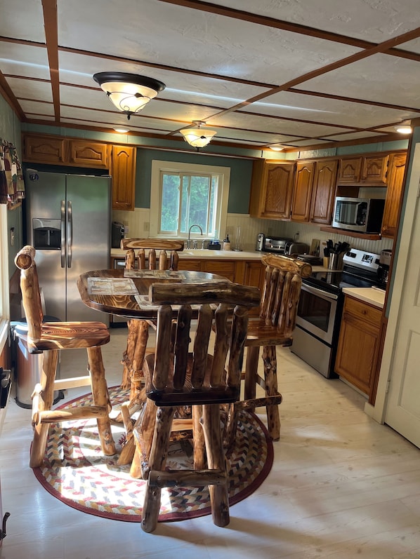A kitchen with wooden cabinets, a stainless steel refrigerator, a microwave, and a wooden dining table with chairs. - Cozy Chalet with First Lake access just minutes from town.  Great Location (Old Forge)