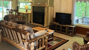 A spacious living room with a large wooden sofa, a fireplace, a mounted deer head, and a ceiling fan. - Cozy Chalet with First Lake access just minutes from town.  Great Location (Old Forge)