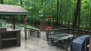 A wooden deck with a gazebo, picnic tables, and a barbecue area surrounded by dense forest. - Cozy Chalet with First Lake access just minutes from town.  Great Location (Old Forge)