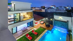 Un edificio residencial moderno de varios pisos con piscina en la azotea, zona de estar al aire libre e interiores bien iluminados.