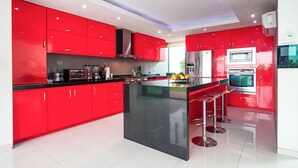 Cocina moderna con armarios rojos, una isla negra, electrodomésticos de acero inoxidable y una barra con taburetes.