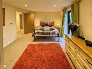 A bedroom with a bed, a dresser, a nightstand, a window with curtains, and a door.
