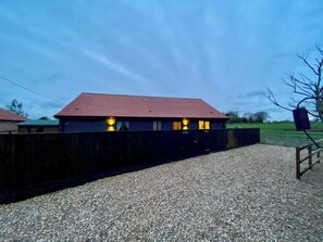 A building with a red roof, a gravel driveway, and a wooden fence.