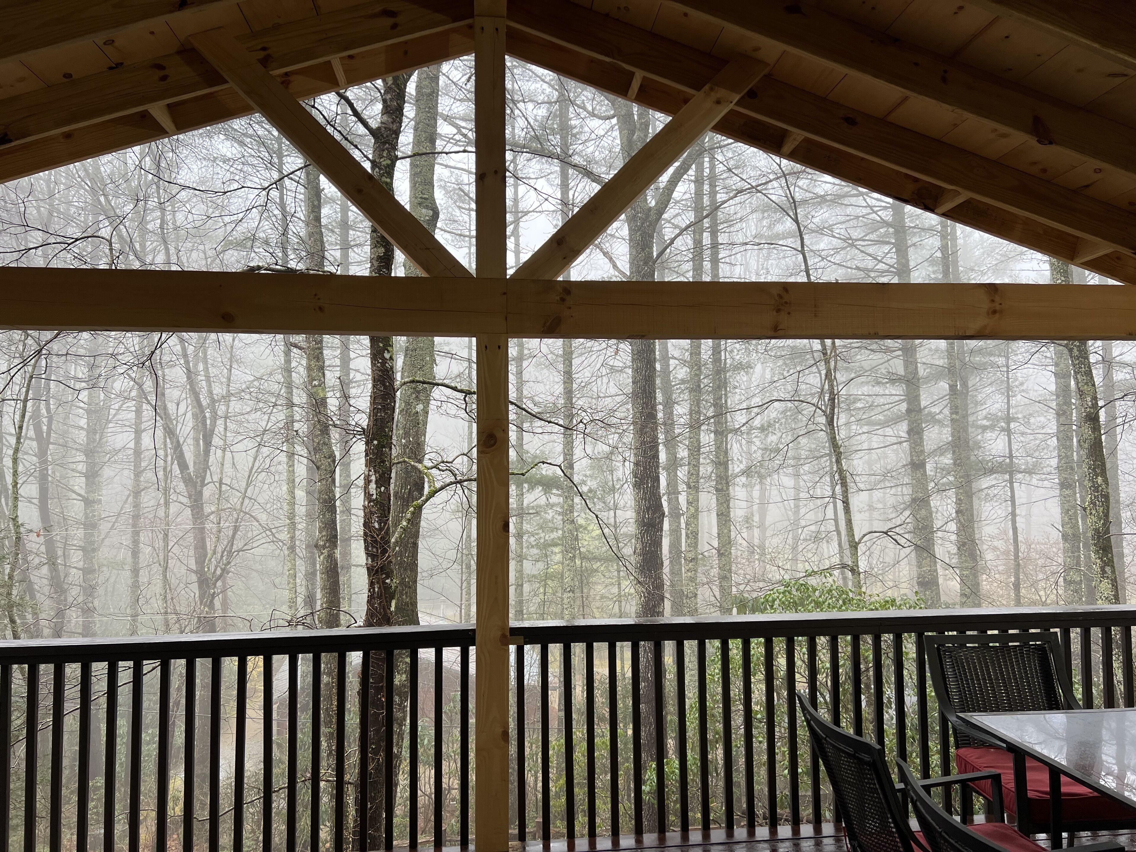 A covered outdoor area with a wooden ceiling and a view of a forest through a window.