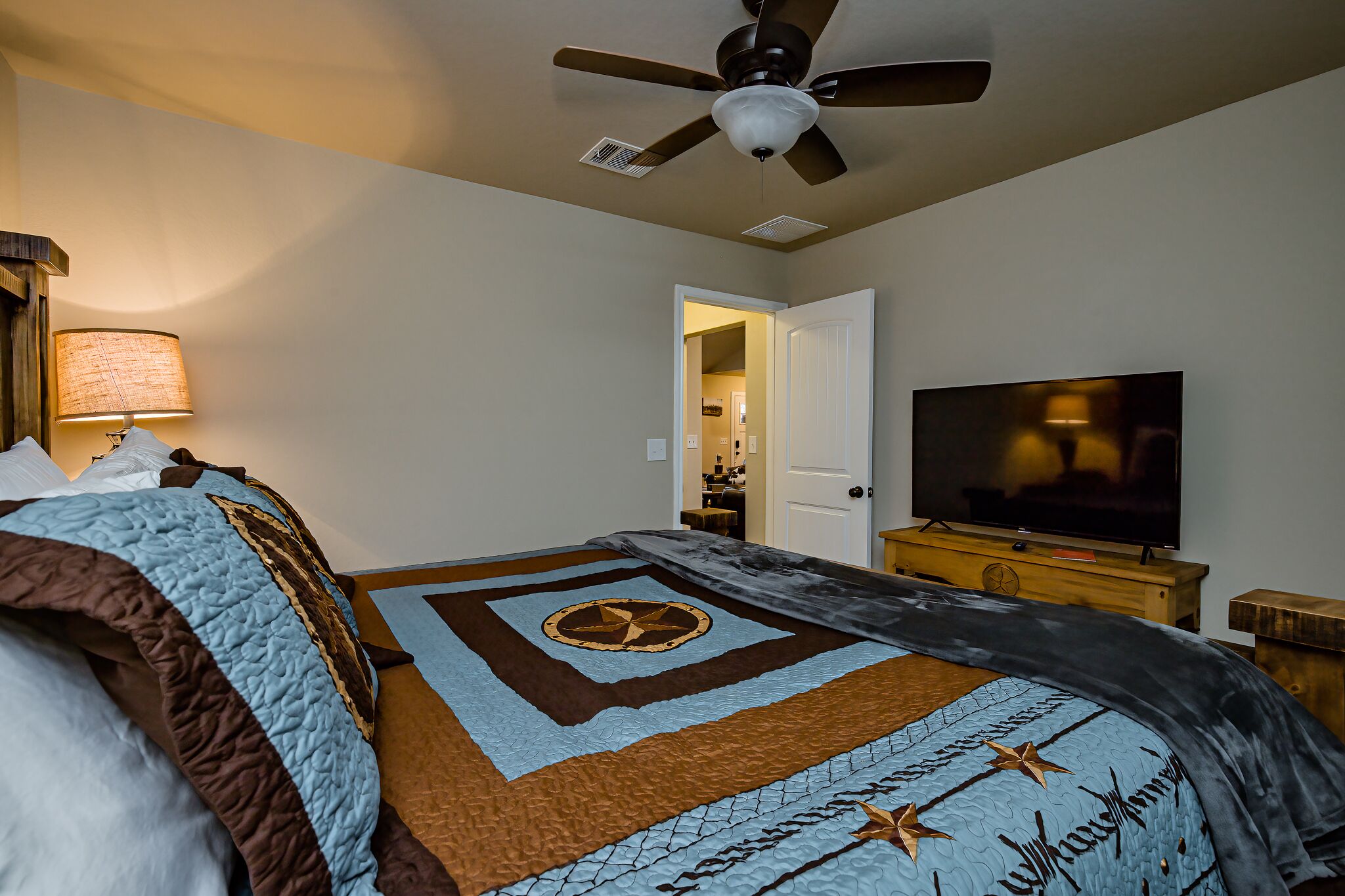 A bedroom with a bed, a ceiling fan, a television, and a door leading to another room.