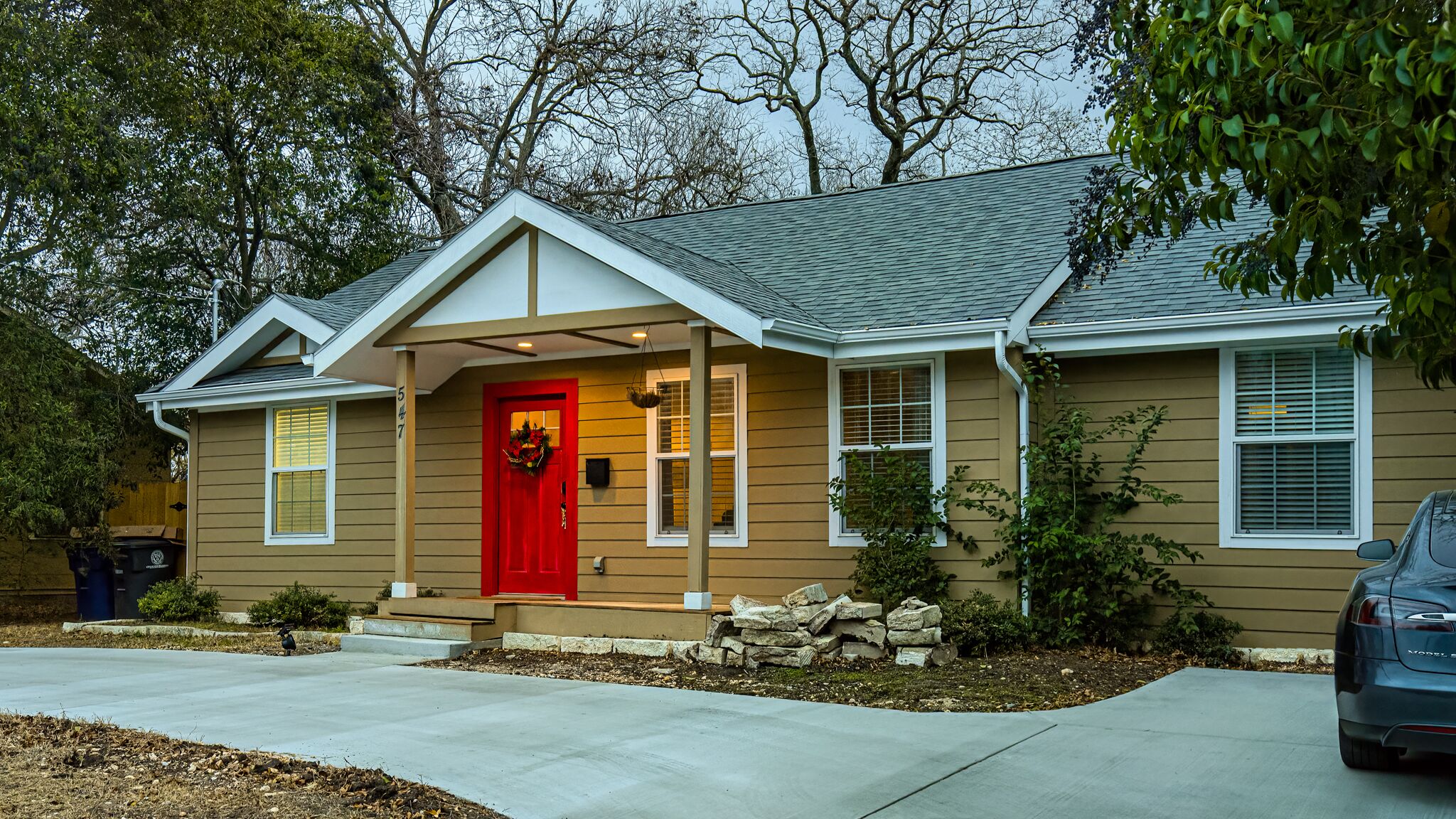 Une maison à deux étages avec une porte d’entrée rouge, un porche couvert et un garage.
