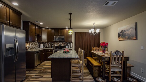 A modern kitchen with a central island, stainless steel appliances, and a dining area with wooden furniture.