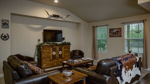 A living room with leather furniture, a wooden cabinet, a mounted buffalo horn, and a large window with blinds.