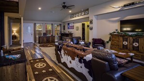 A spacious living room with a large leather sofa, a wooden coffee table, and a TV mounted on the wall.