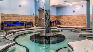 A pool area with a central fountain, seating along the pool, and a door in the background. - Upgraded Cozy 3 Bdrm Corner Suite, Great Mountain Views, Resort and Spa (Canmore)