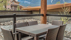 A terrace with wicker furniture, a stone wall, and a mountain view. - Upgraded Cozy 3 Bdrm Corner Suite, Great Mountain Views, Resort and Spa (Canmore)