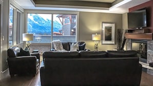 A living room with a large window, a fireplace, and a television. - Upgraded Cozy 3 Bdrm Corner Suite, Great Mountain Views, Resort and Spa (Canmore)