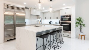 Una cocina moderna con una isla grande, electrodomésticos de acero inoxidable e iluminación colgante.