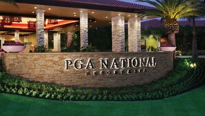 A stone wall with the text "PGA NATIONAL RESORT" and a covered outdoor area with palm trees and a red-tiled roof.